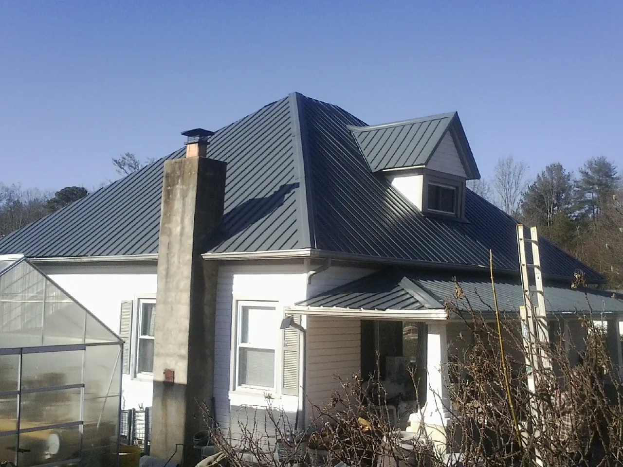 Dark blue standing seam metal roof on a white farmhouse with dormer — Slate & Tile Roof Repair by Roofing Brothers in Liberty